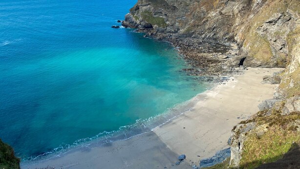 Un paysage côtier avec une plage, une eau d’un bleu limpide et des falaises rocheuses.