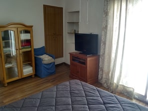 A bedroom with a bed, a wardrobe, a television on a wooden stand, and a window with curtains.