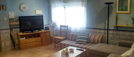 Una sala de estar con televisión, muebles de madera, un ventilador y un sofá.