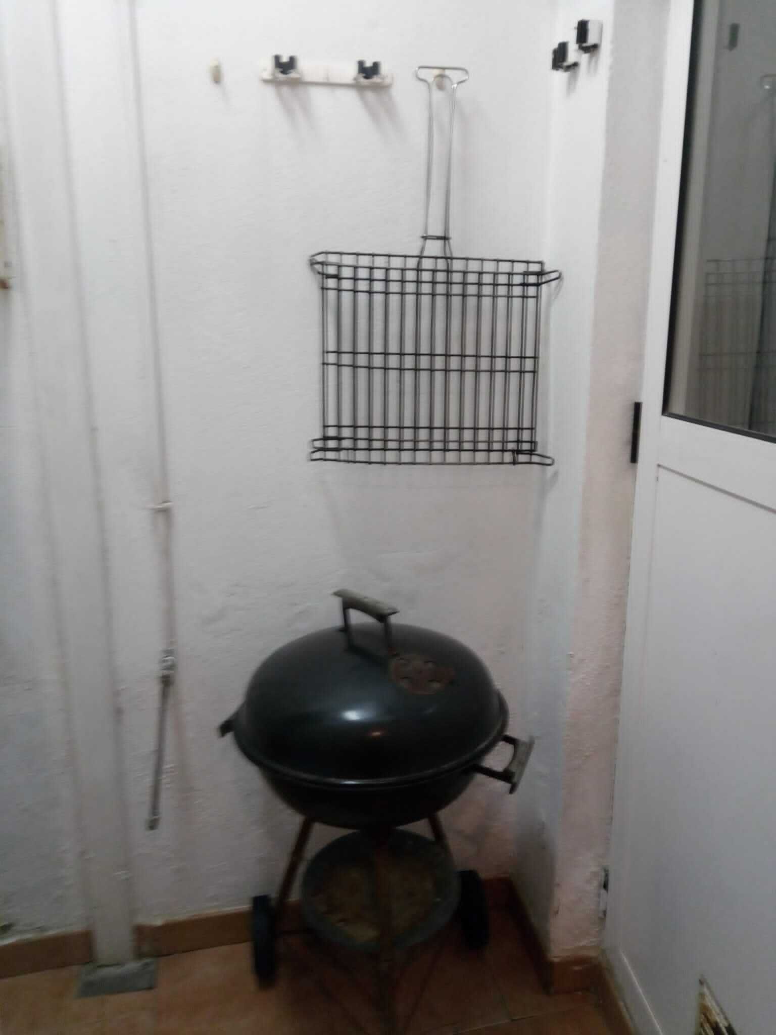 A small, enclosed space with a black barbecue grill, a metal rack on the wall, and a door.