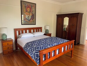 Une chambre à coucher avec un lit en bois, deux tables de chevet, une commode, une armoire et un tableau au mur.