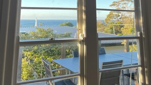 A room with a large window overlooking a coastal area, including a lighthouse and trees. - McCrae: location, location! Boasting  bay views with the beach a 5 minutes walk. (McCrae)