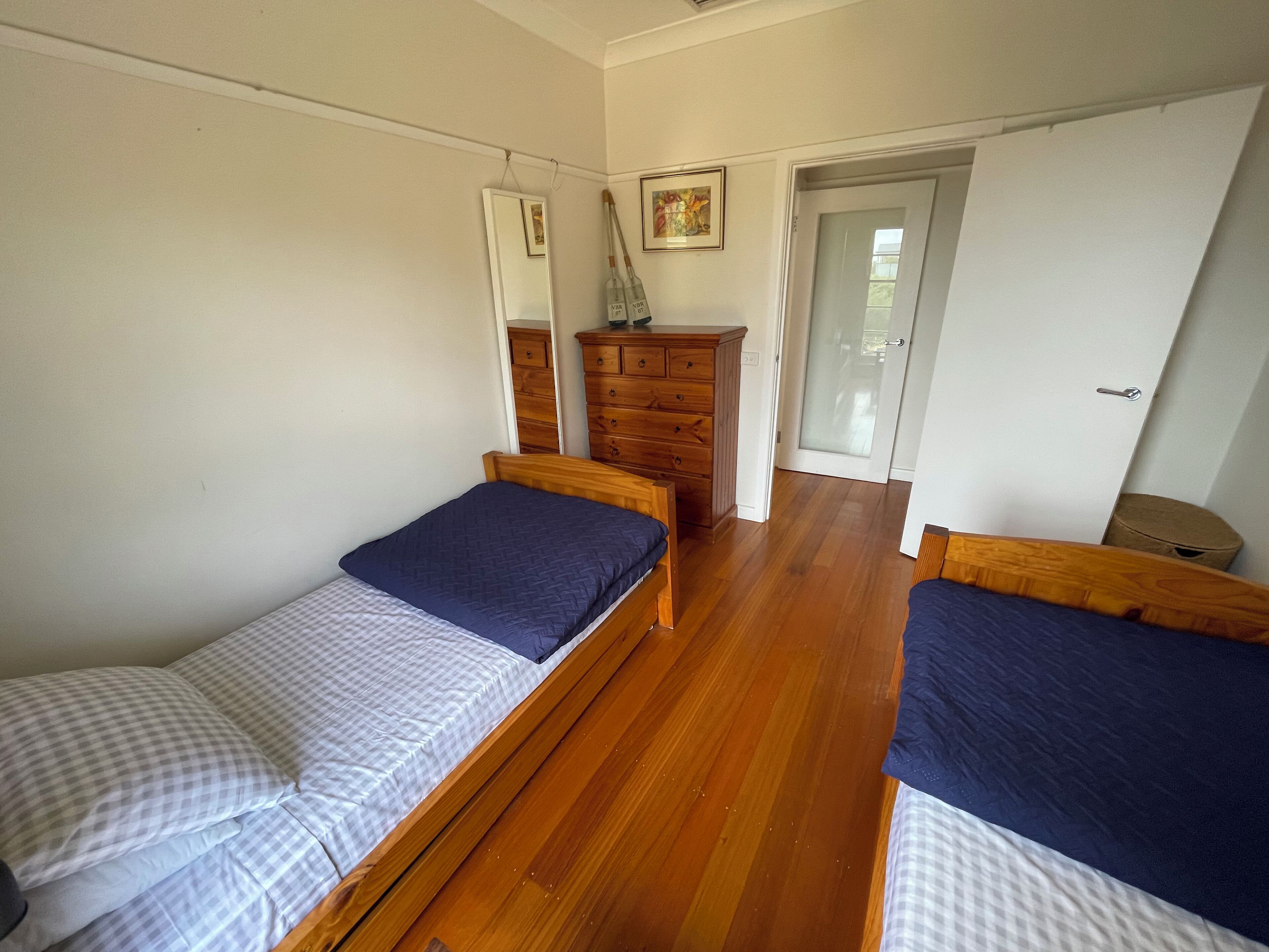 Ein Schlafzimmer mit zwei Holzbetten, einem Schminktisch, einem Spiegel und einer Tür zu einem anderen Raum.