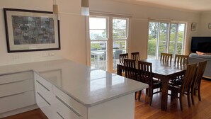 A modern kitchen with a large island, wooden dining table, and chairs. There are large windows providing natural light and views of the outdoors. - McCrae: location, location! Boasting  bay views with the beach a 5 minutes walk. (McCrae)