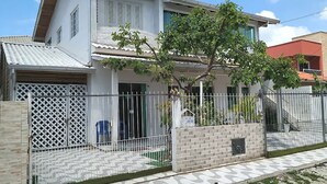 A two-story house with a white exterior, a tiled roof, and a fenced front yard. - Beach House Great Value (Ingleses Norte)