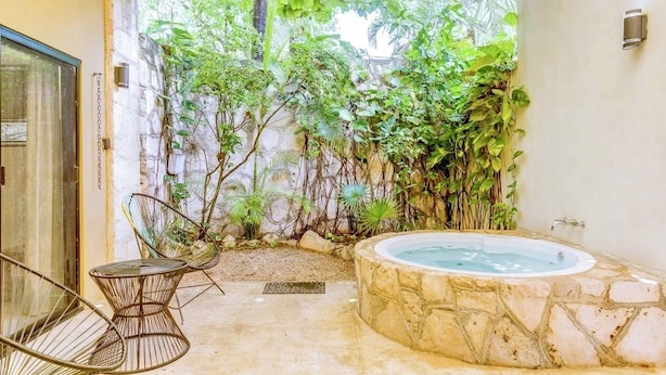 A private patio with a stone hot tub, a glass door, and a seating area with chairs. - Nestled in the heart of Tulum town, steps away from Tulum's most lively street (Tulum)
