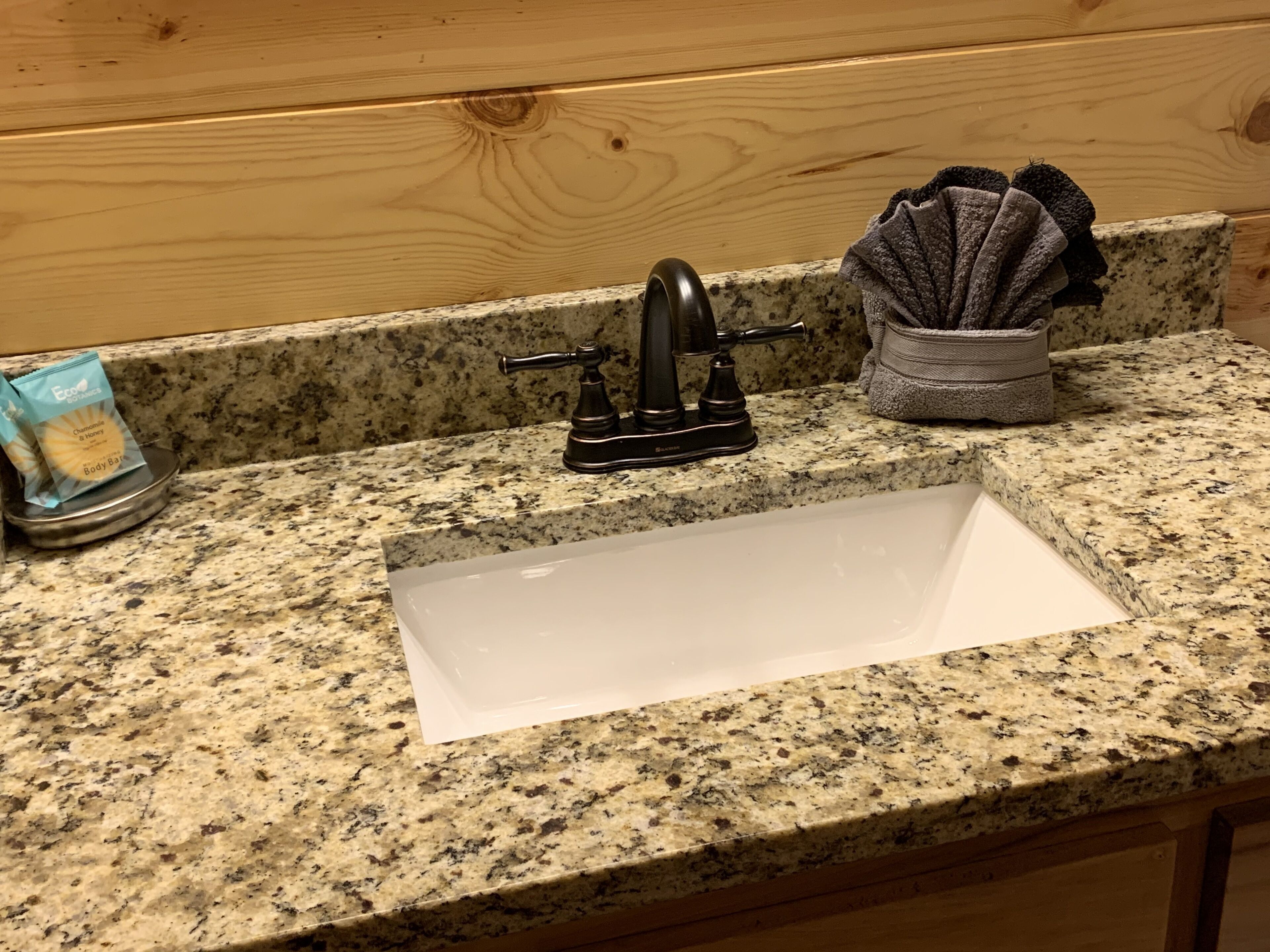 A kitchen with a granite countertop, a white sink, a black faucet, and a small basket with a cloth.
