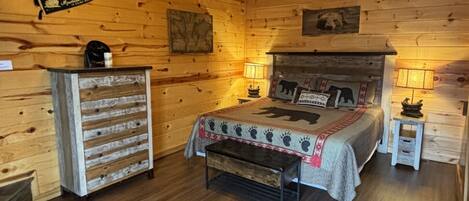 Ein gemütliches Schlafzimmer in einer Blockhütte mit Bett, Schminktisch, Deckenventilator und Kamin.
