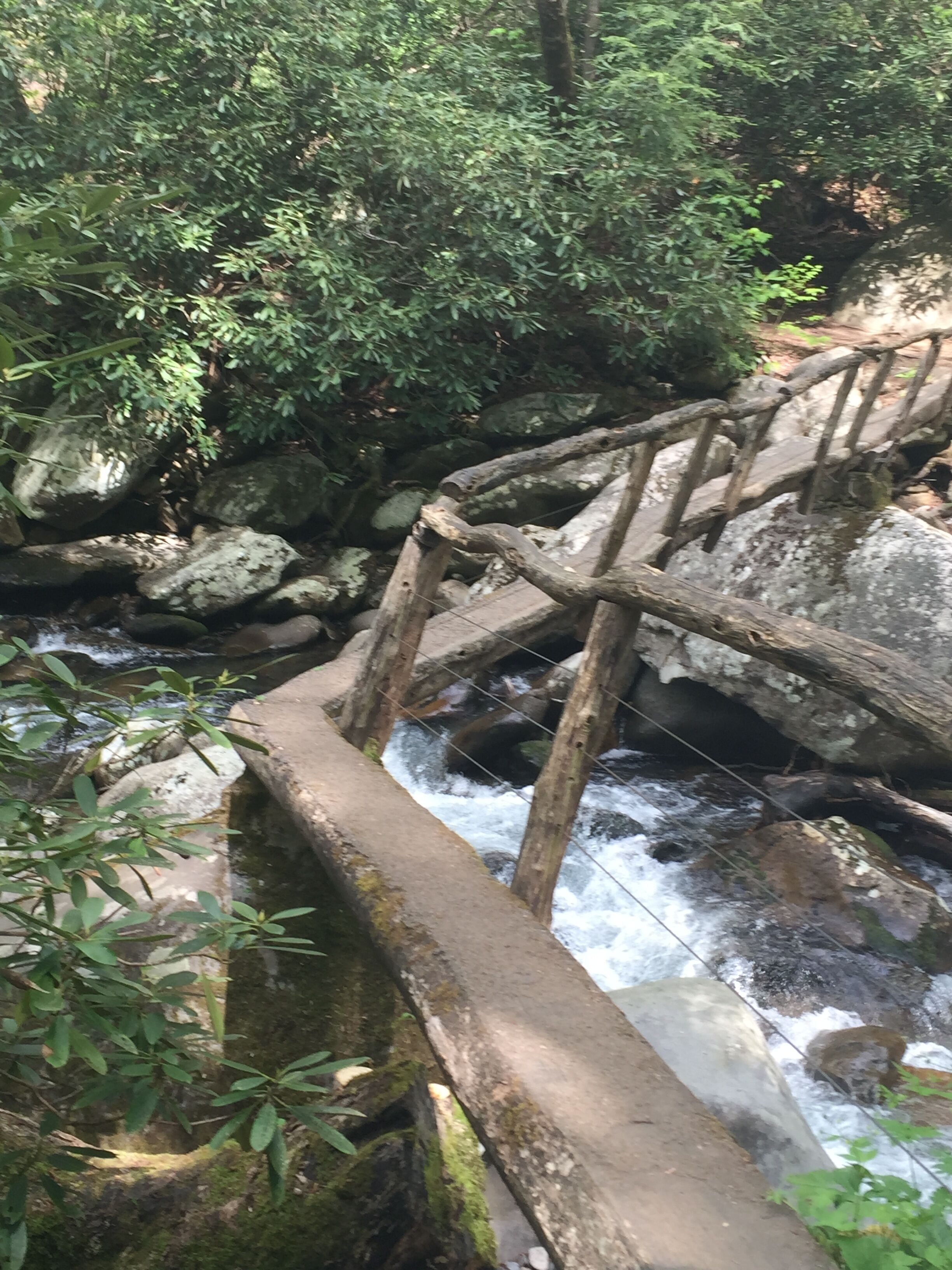 Eine Steinbrücke über einem plätschernden Bach in bewaldeter Landschaft.