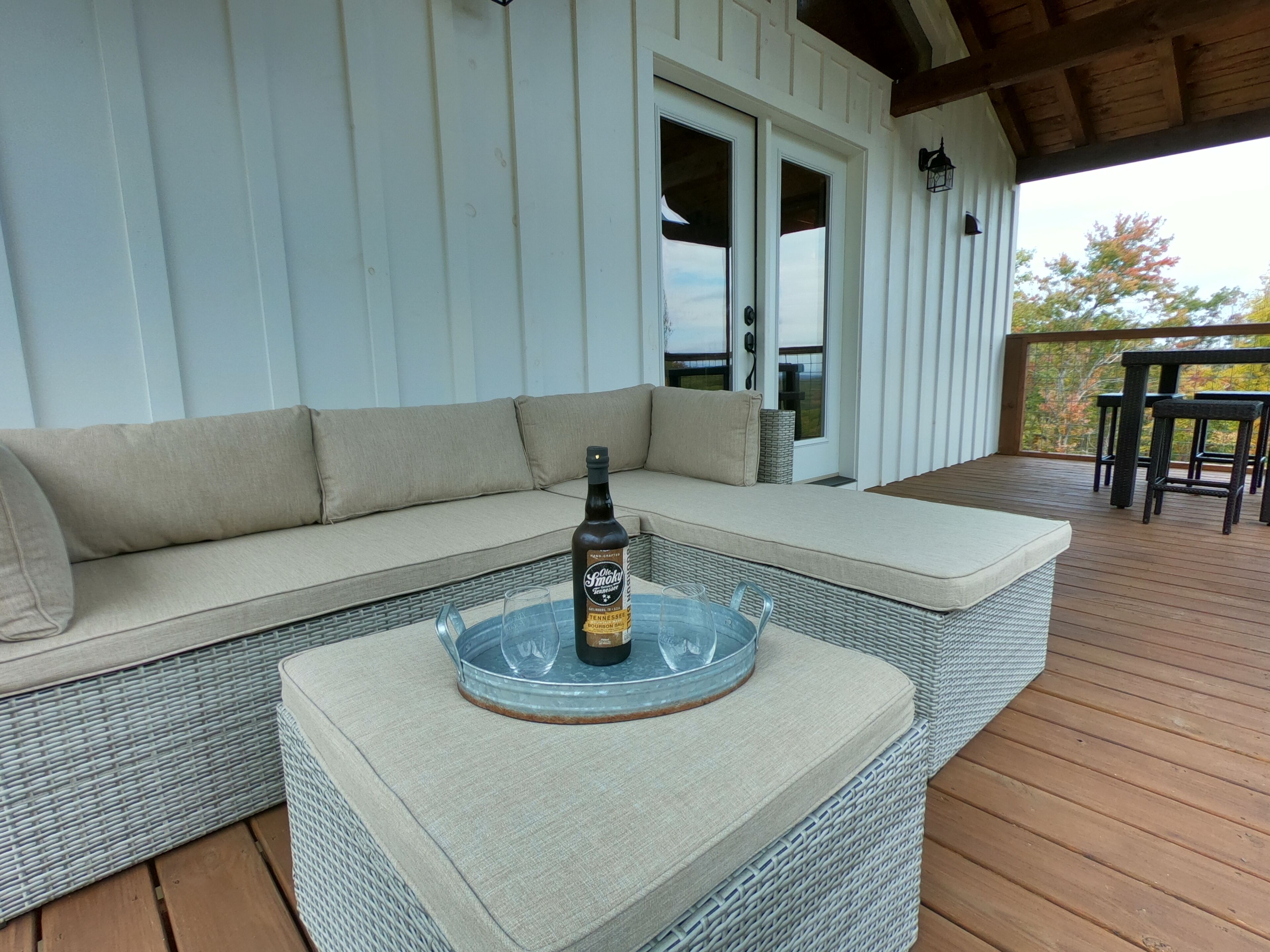 A covered outdoor seating area with a cushioned sofa and a small table with a bottle and glass.