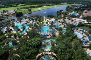 An aerial view of a resort with multiple swimming pools, palm trees, and a golf course.