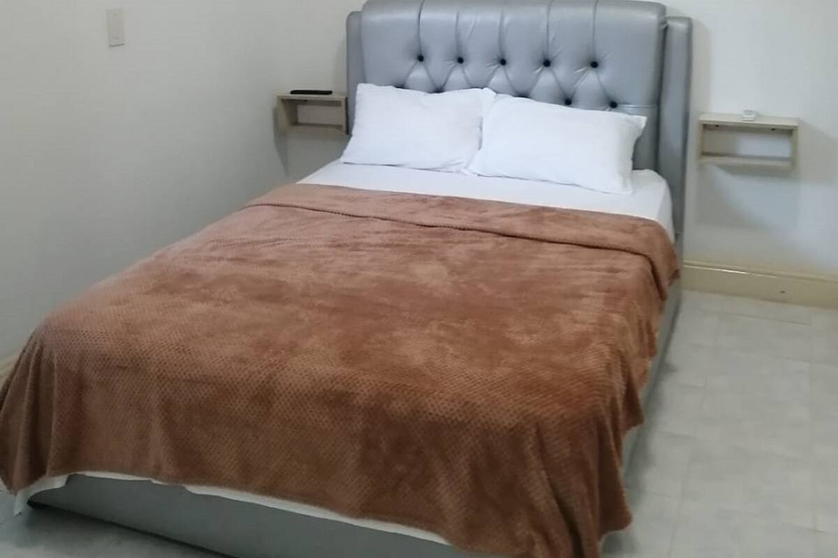 A single bed with a tufted headboard, white bedding, and a brown throw blanket. There are two bedside tables, one on each side of the bed.
