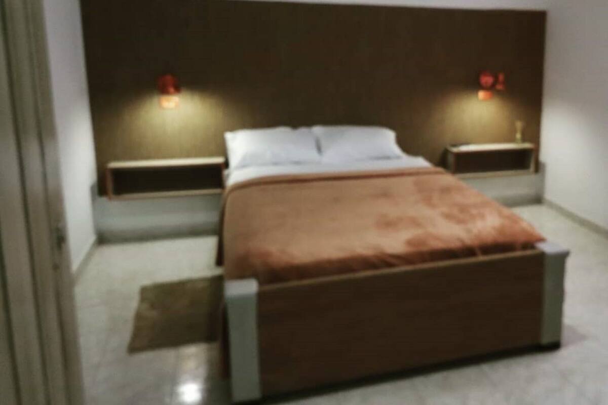 A bedroom with a bed, two bedside tables, and wall-mounted lights.