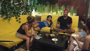 A group of people sitting on a yellow couch and a table with food and drinks. - Hostal La Antigua Capsula (Cali)