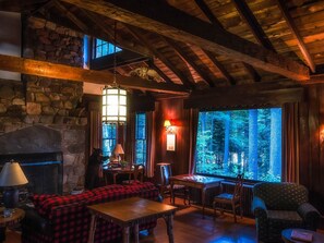 Cozy seating area with a fireplace, sofa, and table, offering a view of the surrounding forest.