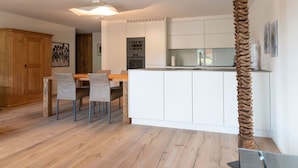 Une cuisine moderne avec des meubles blancs, une table à manger en bois avec des chaises, et une sculpture en bois originale.