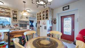 A kitchen with a dining table, chairs, a chandelier, and a red door with a decorative glass panel. - BYRD'S FARMHOUSE CHICK-INN COOP (Shiner)