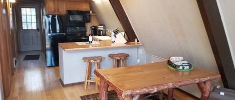 A kitchen with wooden cabinets, a microwave, and a coffee maker. There is a wooden table with two stools and a bench.