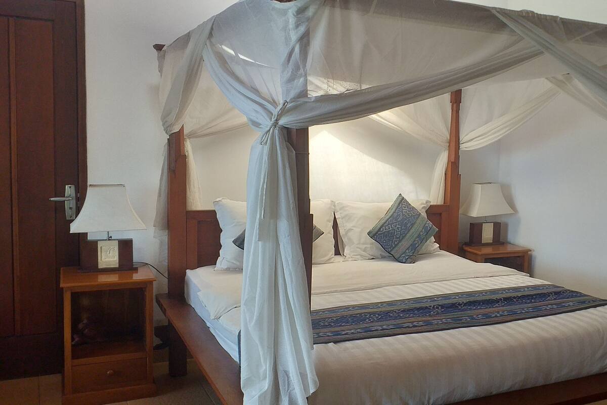 A four-poster canopy bed with white linens and a blue patterned throw.