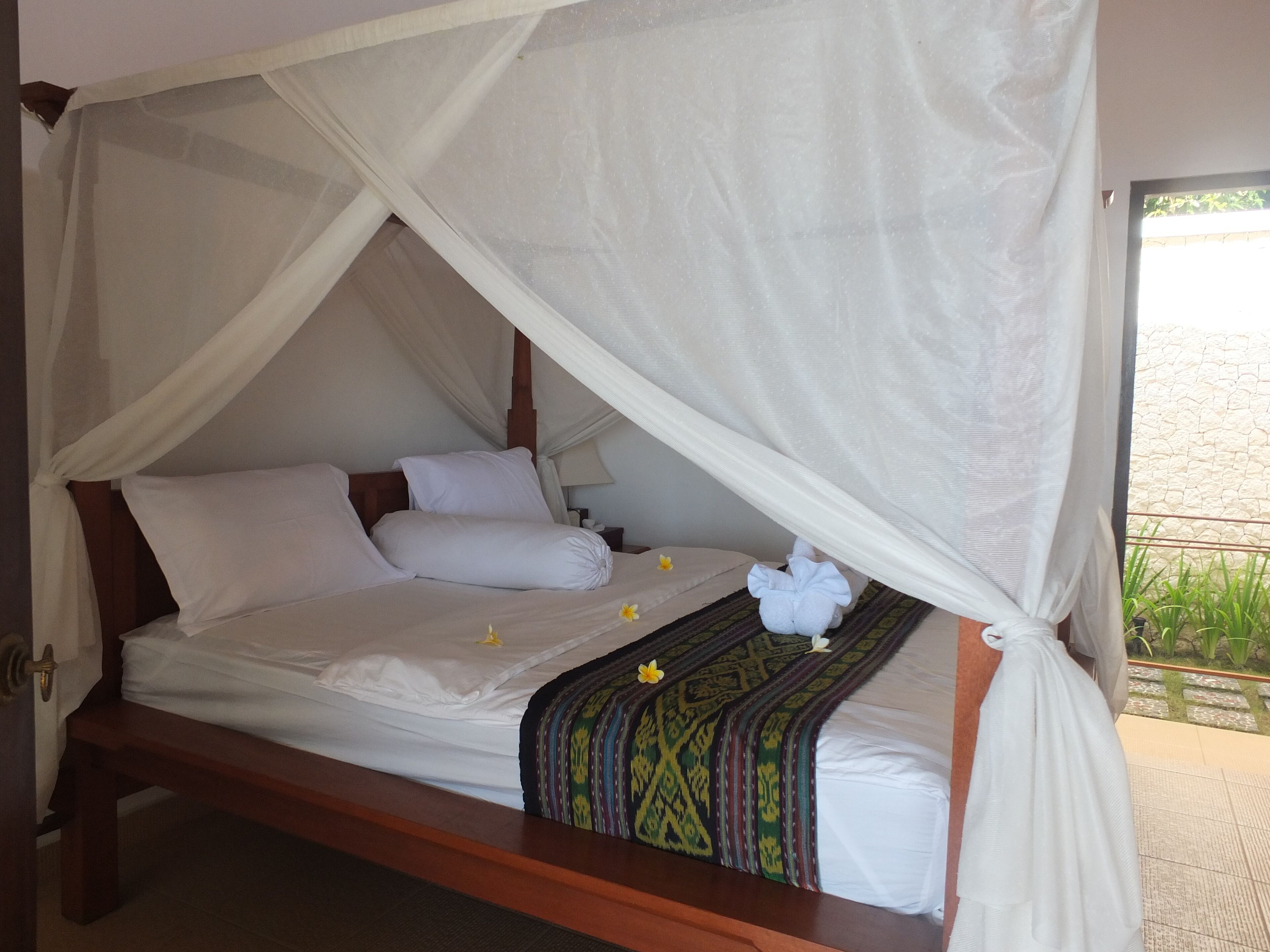 A bed with a canopy, white bedding, and a decorative pillow.