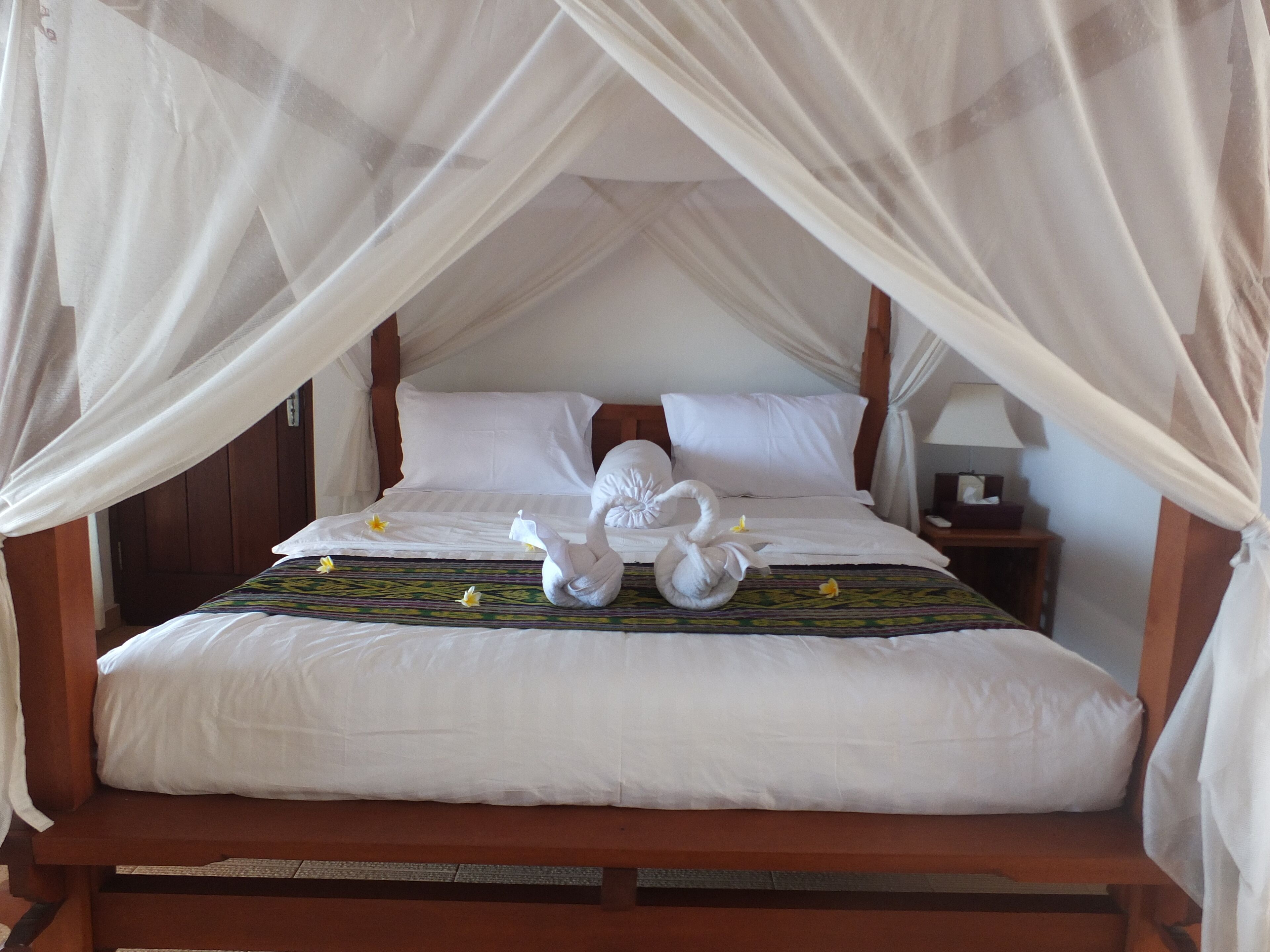 A bed with a canopy, white pillows, and a bedspread with a floral pattern.