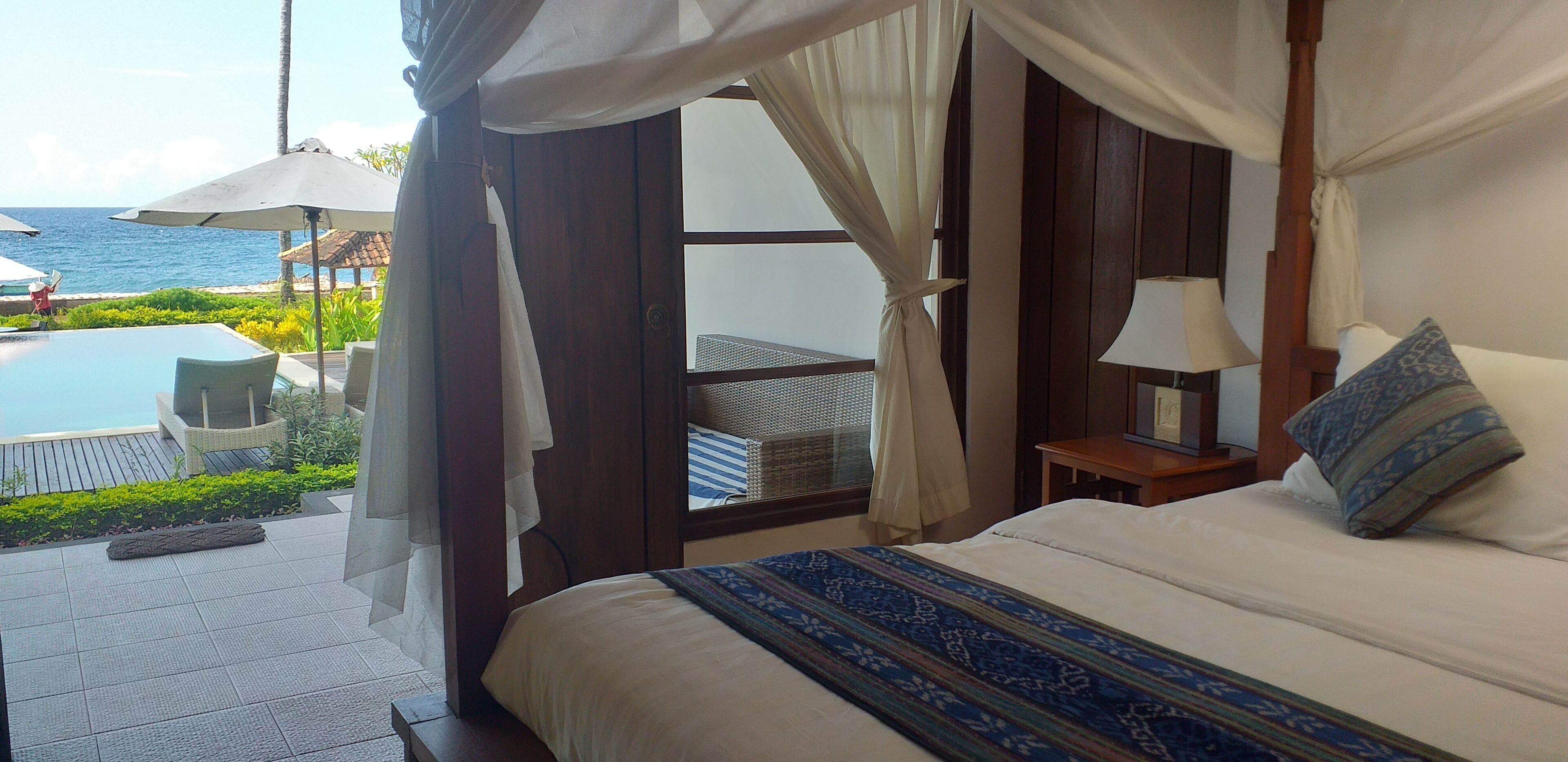 A bedroom with a large bed, a nightstand, a lamp, and a view of the ocean.