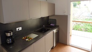 Eine kompakte Küche mit integriertem Geschirrspüler, einer Kaffeemaschine und einem Fenster mit Blick ins Freie.