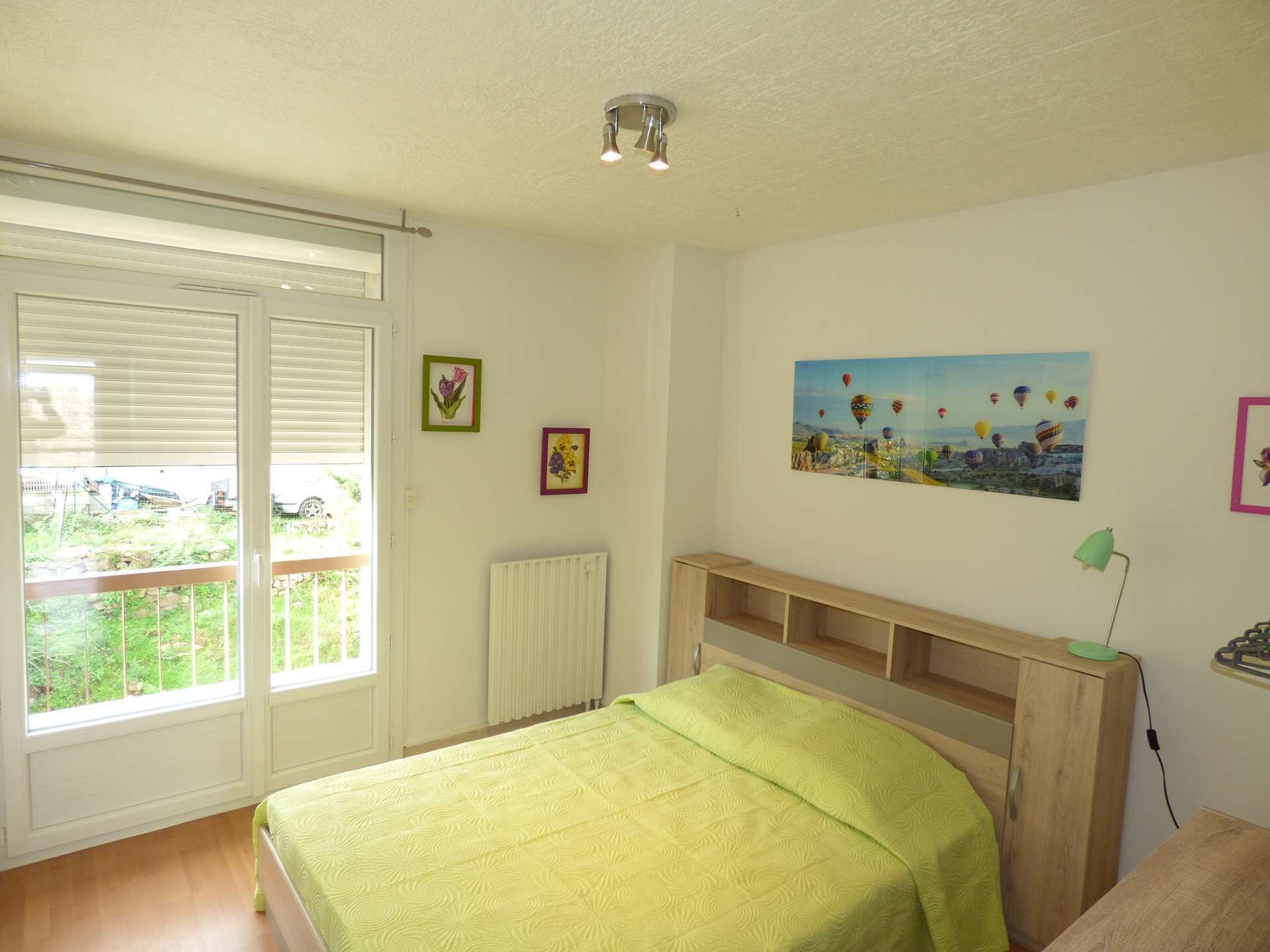 Une chambre à coucher avec un lit, un radiateur, une fenêtre avec des stores et un tableau représentant des montgolfières accroché au mur.