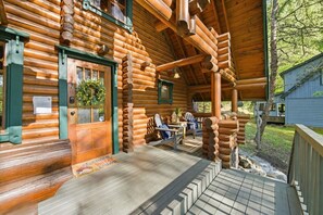 A log cabin with a porch, a wooden door, and a seating area with a table and chairs. - Cozy Log Cabin with Private Hot Tub Soaky Mtn (Sevierville)