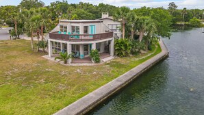 A two-story house with a balcony, surrounded by lush greenery and a canal.