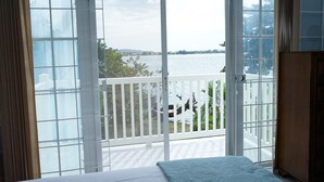 Une pièce dotée d’une grande porte-fenêtre coulissante donnant sur un balcon avec vue sur une étendue d’eau et des bâtiments éloignés.