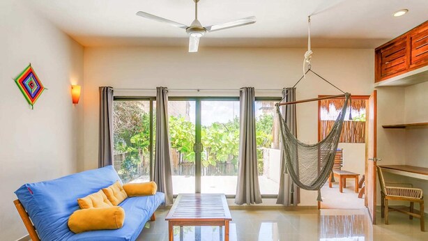 A modern living room with a blue sofa, a wooden coffee table, and a hammock. - Experience Tulum’s laidback yet vibrant lifestyle in this cozy apartment (Tulum)