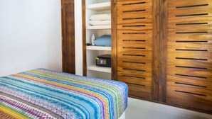 A bedroom with a colorful bedspread, a wooden wardrobe with multiple shelves, and a small ironing board. - Experience Tulum’s laidback yet vibrant lifestyle in this cozy apartment (Tulum)