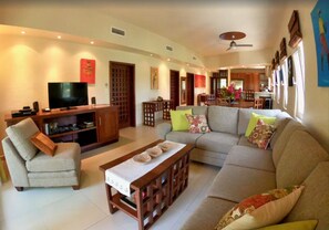 A living room with a sofa, armchairs, a coffee table, a TV, and a dining area with chairs and a table.
