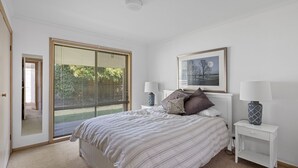 Een slaapkamer met een groot bed, twee nachtkastjes met lampen, een inlijsting foto aan de muur en een schuifdeur van glas die leidt naar een balkon.