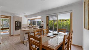 Een moderne keuken met een centraal eiland, een eetgedeelte met houten stoelen en grote ramen met uitzicht op groen.