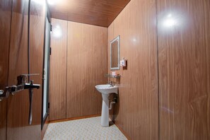A bathroom with wooden walls, a white pedestal sink, a mirror, and a shower with a handheld showerhead. - Garden Villa - Hostel (Ha Giang 1)