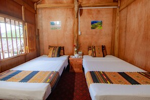A wooden room with two beds, each with patterned bedding, a small table with a vase and a teapot, and two framed pictures on the walls. - Garden Villa - Hostel (Ha Giang 1)