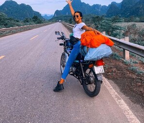 A person sitting on a motorcycle with a license plate on a road with mountains in the background. - Garden Villa - Hostel (Ha Giang 1)