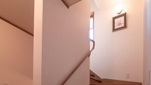 Una escalera de madera con barandilla, un accesorio de iluminación en la pared y un cuadro enmarcado sobre los escalones.
