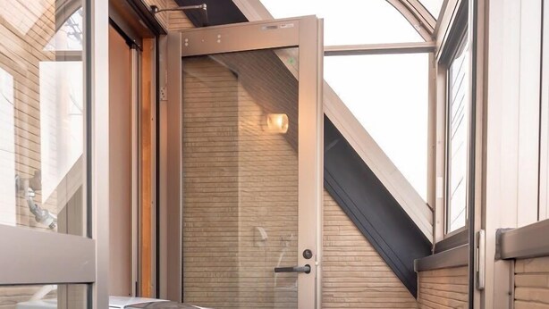 Un pasillo estrecho con un electrodoméstico blanco, un panel de madera y una puerta que da a una habitación con techo inclinado.