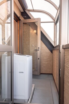 Un pasillo estrecho con un electrodoméstico blanco, un panel de madera y una puerta que da a una habitación con techo inclinado.