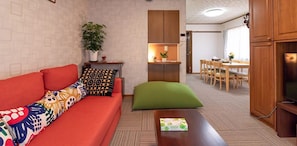 A modern living room with a sofa, a small table, and a dining area in the background.