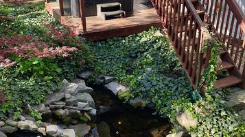 A wooden deck with a hot tub and a small pond surrounded by rocks and greenery.