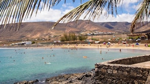 A beach with clear water, people swimming, and a stone wall in the foreground.