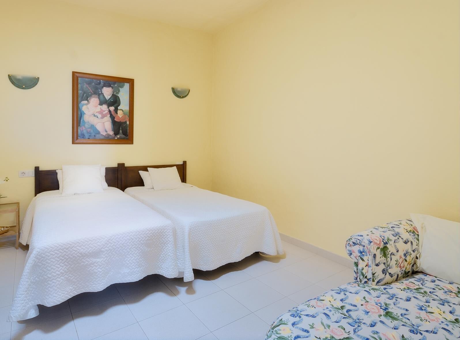 Een kamer met twee eenpersoonsbedden, een kleine zithoek, een schilderij aan de muur en een betegelde vloer.