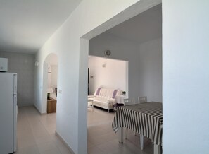 A modern, minimalist living space with a dining area, a sofa, and a kitchen.