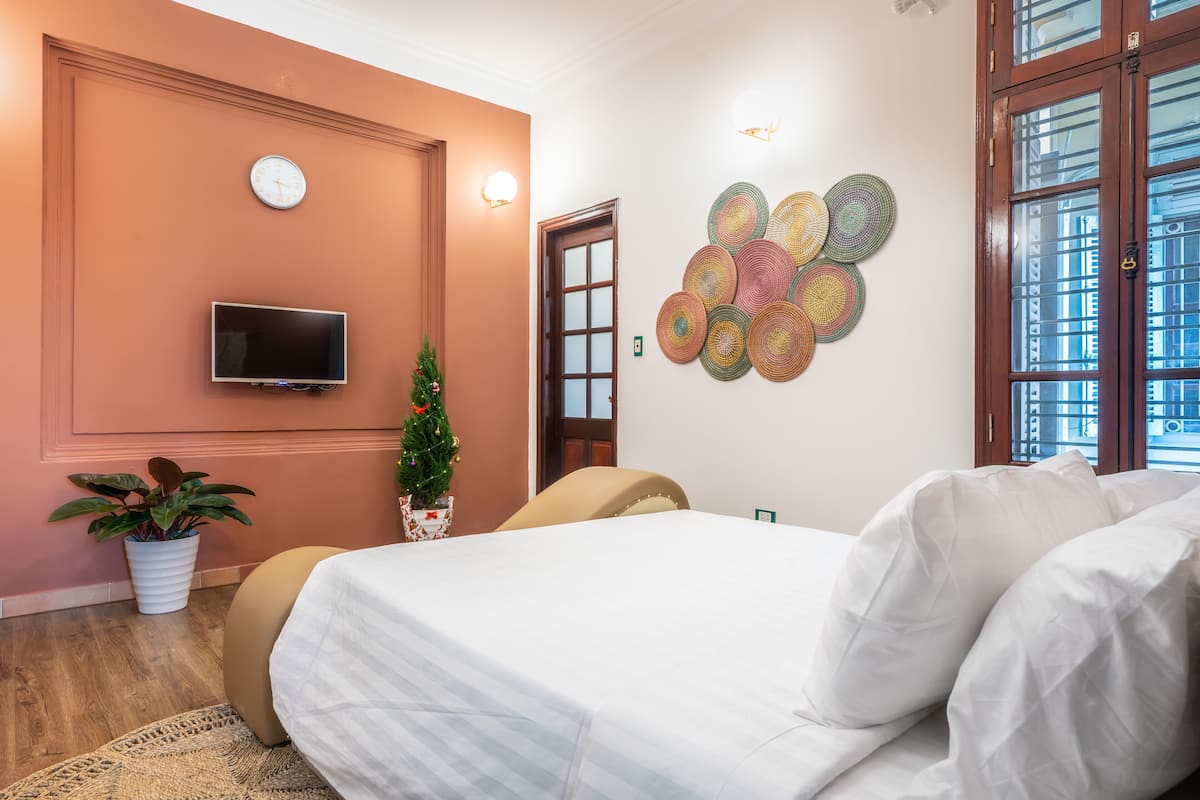 A bedroom with a bed, a television, a clock, a wall art piece, and a window.