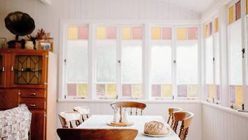 A dining room with a wooden table set for four, a cabinet with a decorative top, and a window with multicolored panes.