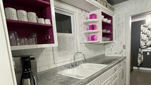 Cozinha moderna com armários brancos, lava-louças de aço inoxidável, pia dupla e máquina de café.